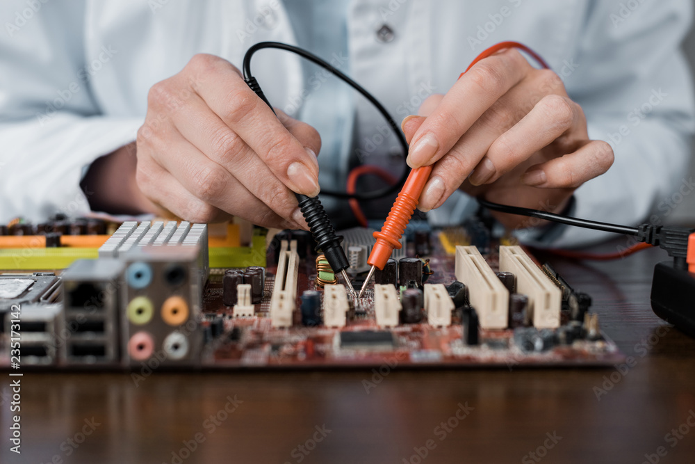 cropped shot of computer engineer with tester examining motherboard cropped shot of computer engineer with tester examining motherboard