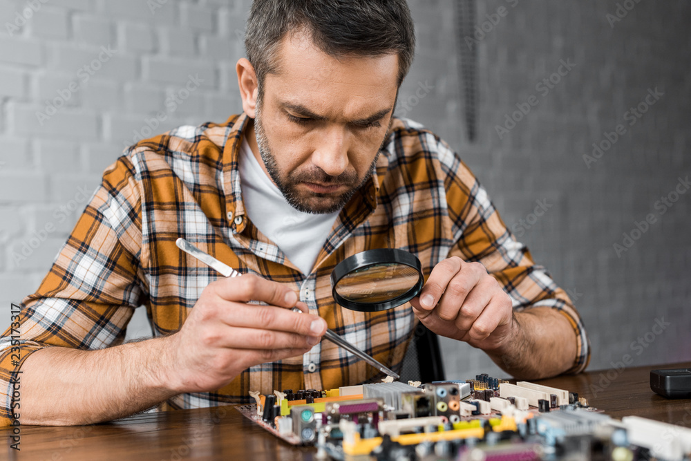 close-up portrait of concentrated electronics engineer with tweezers and magnifying glass repairing motherboard close-up portrait of concentrated electronics engineer with tweezers and magnifying glass repairing motherboard