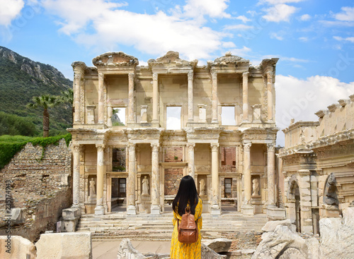A young Asian tourist woman wearing yellow dress enjoying the view at Library of Celsus at Ephesus which is an ancient Roman building in Ephesus, Anatolia and now part of Selçuk, Turkey.