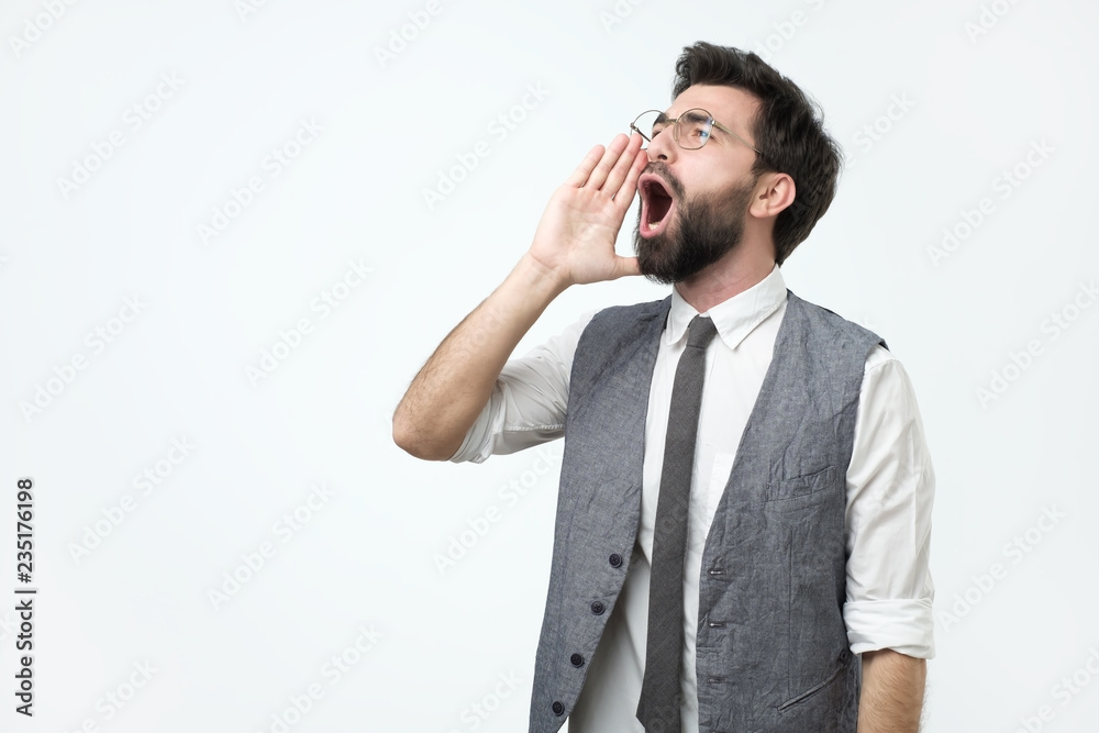 Young hispanic adult man with beard shouting and screaming loud to side with hand on mouth. Communication concept. Young hispanic adult man with beard shouting and screaming loud to side with hand on mouth. Communication concept.