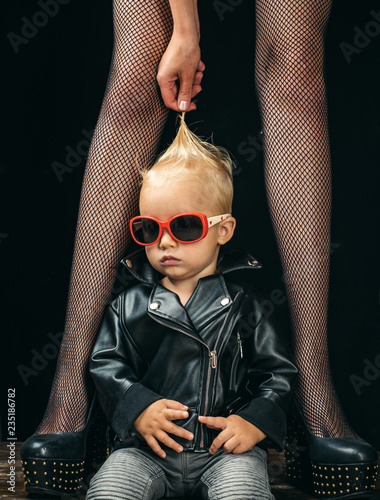 Forever rocker. Rock and roll fashion trend. Small boy at female legs. Rock style child. Cute little music fan. Little rock star. Small child boy in sunglasses and rocker jacket. Music for children