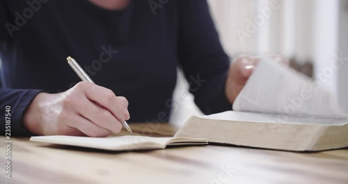 Handheld closeup shot of a woman studying the Bible at home and taking notes.