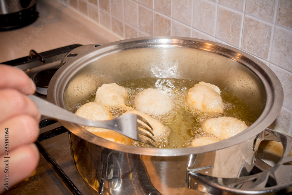 Woman's hands that Adjusting the Dough Friying in a Pot during the Preparation of an Italian Christmas Traditional Dish called Pettole Woman's hands that Adjusting the Dough Friying in a Pot during the Preparation of an Italian Christmas Traditional Dish called Pettole