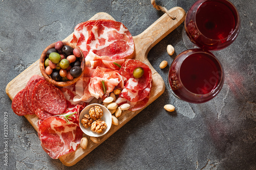 Top view of meat plate, cold smoked pork, jamon, prosciutto, salami served with wine, nuts and olives from above photo