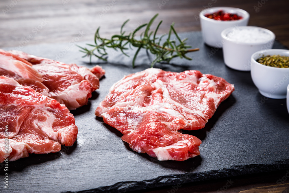 Raw beefsteaks on black stone on wooden background