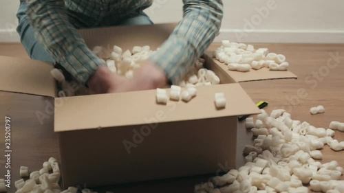 A young woman searching through an open carton box parcel, filled with insulation foam. Low angle static shot.