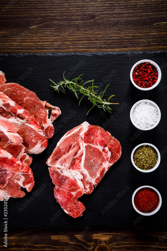 Raw beefsteaks on black stone on wooden background