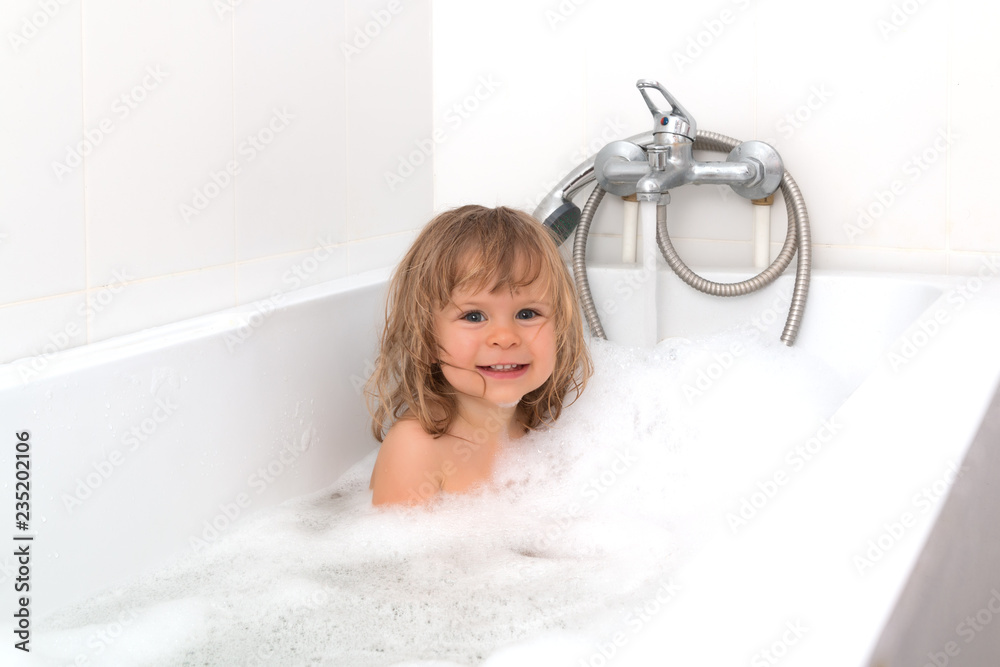 Fun cheerful happy toddler baby taking a bath playing with foam bubbles. Little child in a bathtub. Smiling kid in bathroom on white background. Infant washing and bathing. Hygiene and health care. Fun cheerful happy toddler baby taking a bath playing with foam bubbles. Little child in a bathtub. Smiling kid in bathroom on white background. Infant washing and bathing. Hygiene and health care.