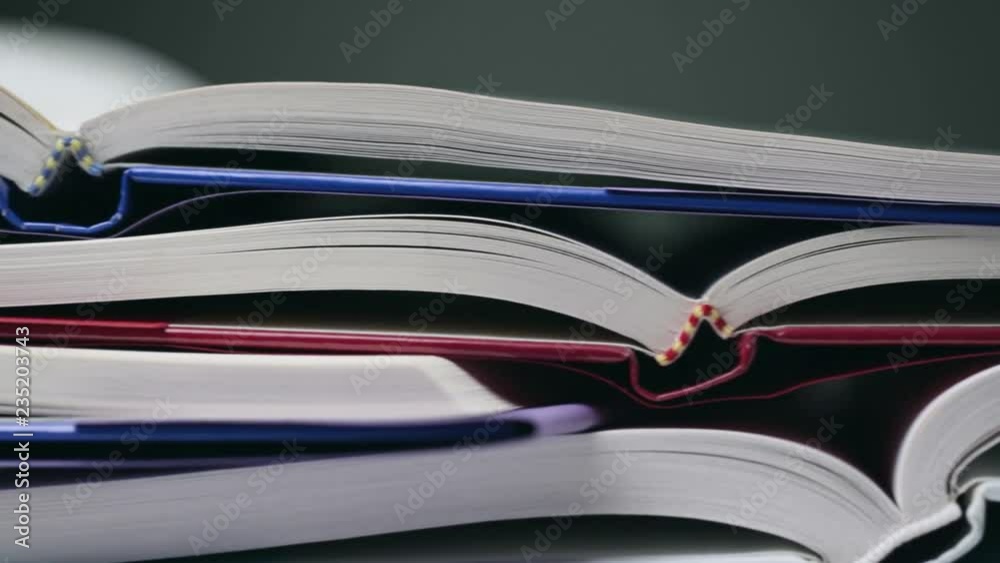 Closeup dolly footage of many open textbooks on a desk. Low angle view.