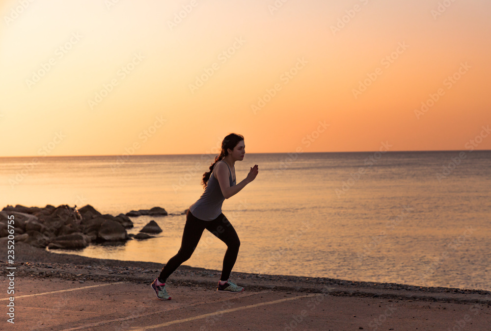Silhouette of running girl on the sunset beach. Healthy lifestyle