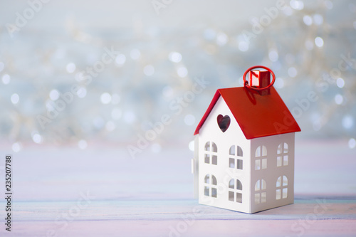 Toy white house with red roof and hole in form of heart on light bokeh background.