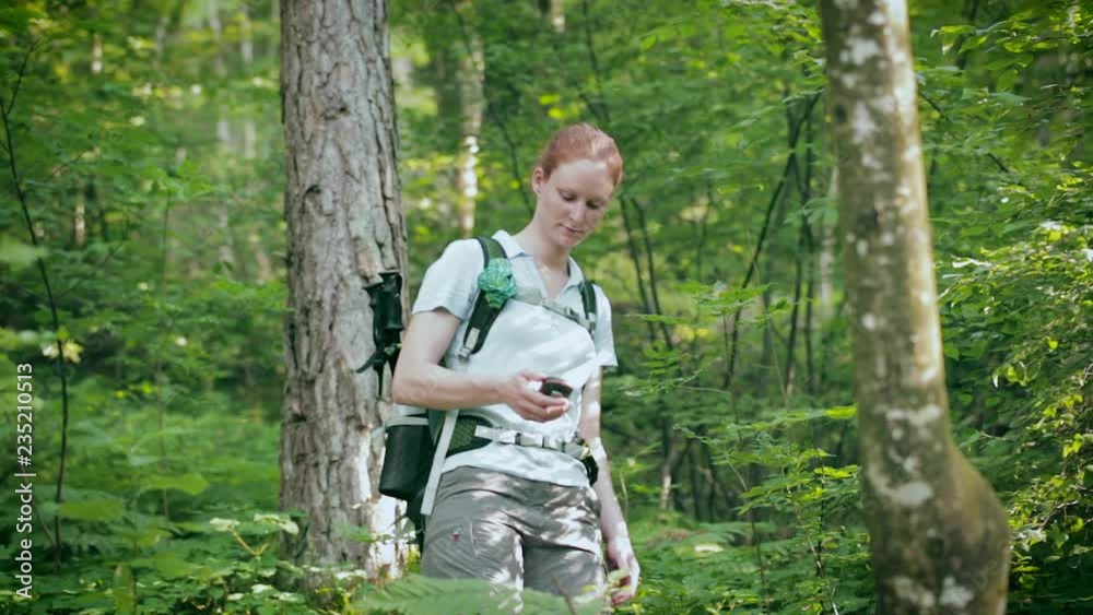 An active female tourist with a backpack and a GPS device hikes in a dense green forest. An active female tourist with a backpack and a GPS device hikes in a dense green forest.