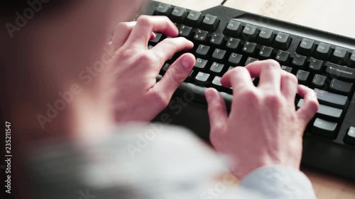 A female office employee types on a computer keyboard. Closeup footage, as seen from behind her shoulder.