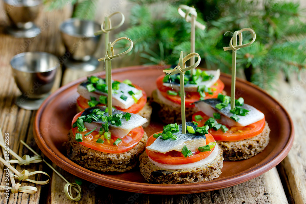Canapes with rye bread, salted herring fillet, mustard, onion, tomato and skewers on plate