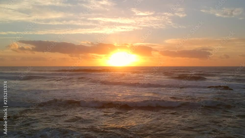 Aerial shot over Atlantic ocean at sunset, moving slowly forward over breaking waves below and orange reflections on water Aerial shot over Atlantic ocean at sunset, moving slowly forward over breaking waves below and orange reflections on water