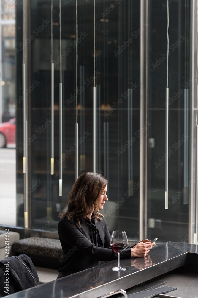 Businesswoman having red wine while using mobile phone in hotel Businesswoman having red wine while using mobile phone in hotel