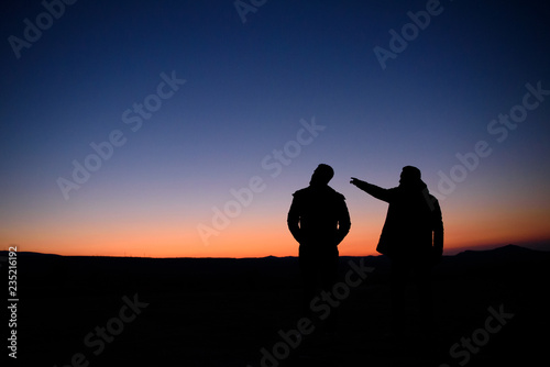 Silhouettes of two people at sunset on the horizon