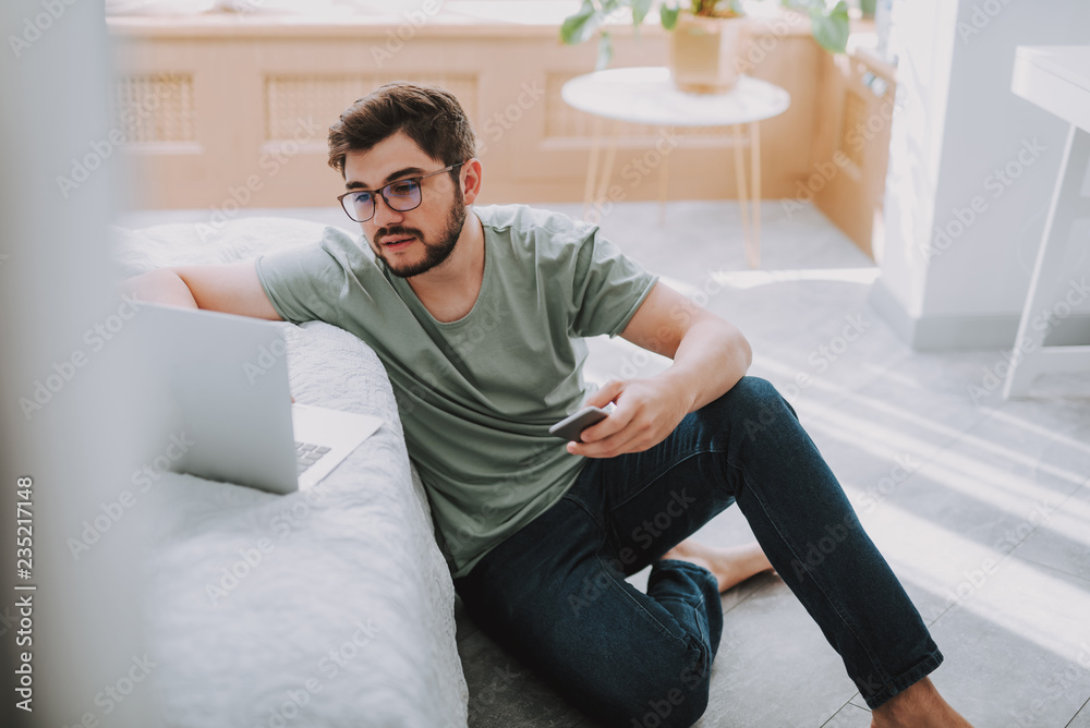 Bearded young man sitting on the floor while surfing the Internet Bearded young man sitting on the floor while surfing the Internet