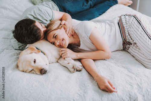 Pleasant young couple having rest in bed while their dog sleeping nearby