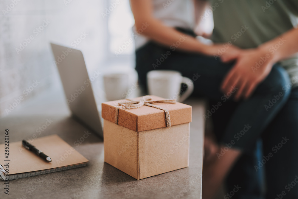 Selective focus of a box with a present inside standing on the table while a passionate couple being in the background Selective focus of a box with a present inside standing on the table while a passionate couple being in the background