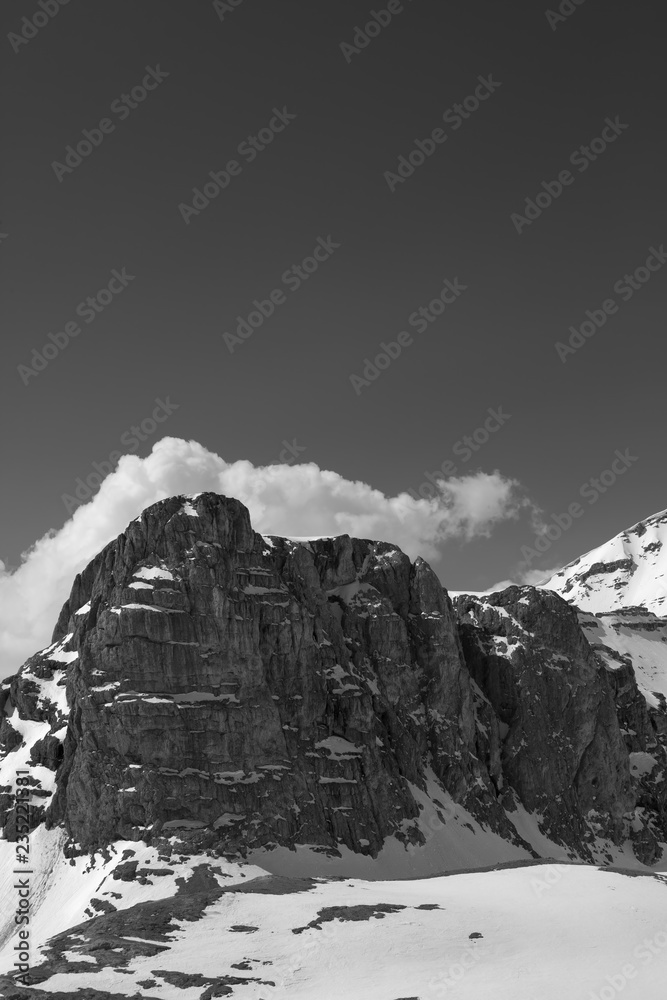 Black and white view on rocks in snow and sky with clouds