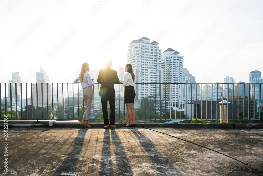 Colleagues chatting in sunset on city rooftop Colleagues chatting in sunset on city rooftop