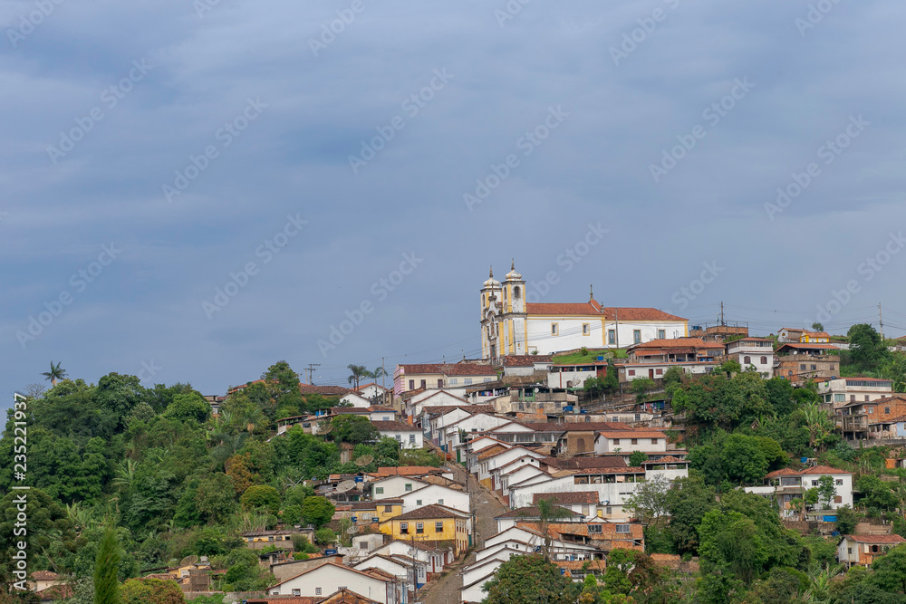 Casarão colonial no centro histórico de Ouro Preto, em primeiro plano, e Igreja de Santa Ifigênia ao fundo com casario em ladeira abaixo, em Ouro Preto, Brasil