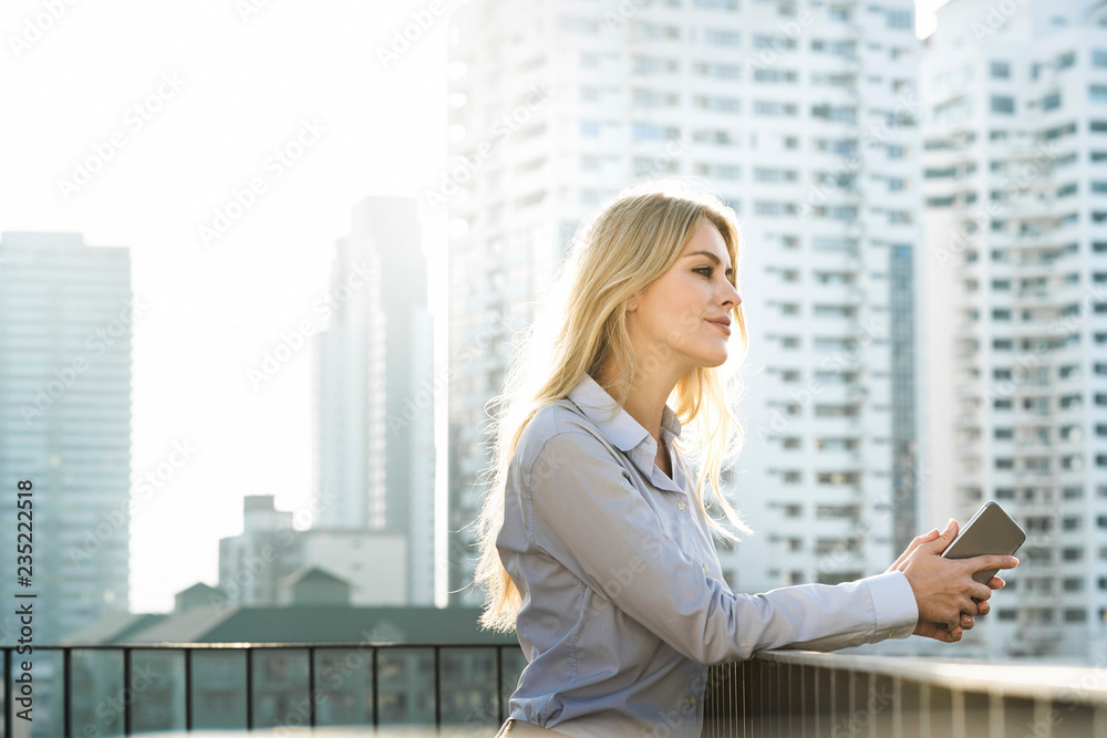 Portrait of blonde business woman leaning onto handrail on city rooftop Portrait of blonde business woman leaning onto handrail on city rooftop
