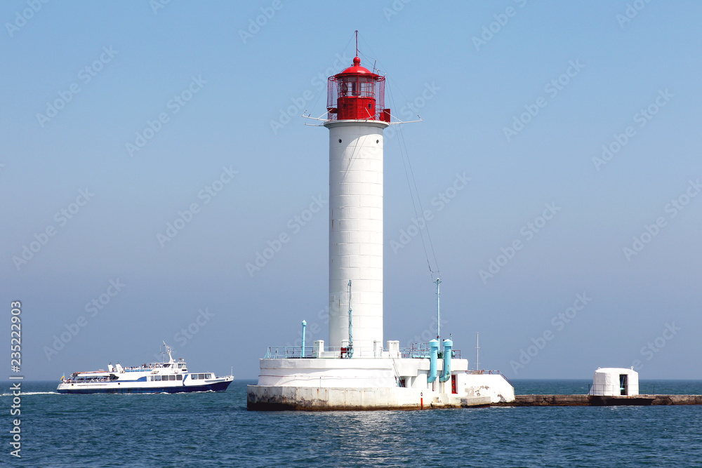 Lighthouse on the sea under the sky. A white sea lighthouse in the middle of the harbor points the path of ships at night and foggy time with light.