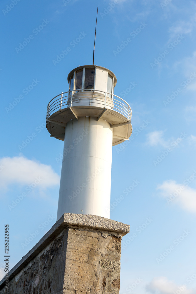 Lighthouse on the sea under the sky. A white sea lighthouse in the middle of the harbor points the path of ships at night and foggy time with light.