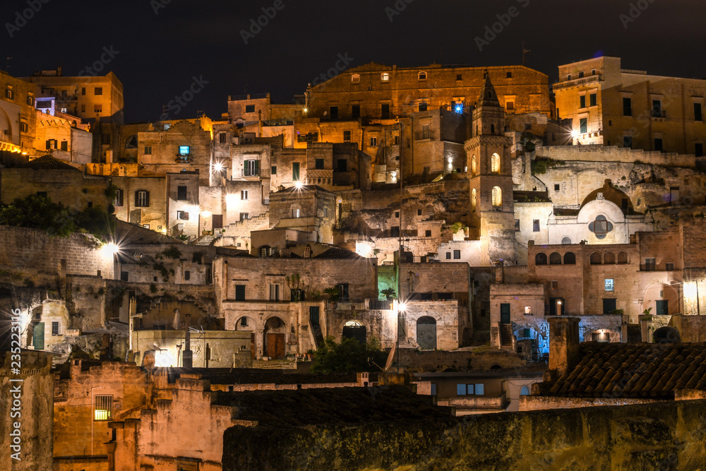 Night view of the old city of Matera, Italy, with it's abandoned hillside homes, church spires and ancient dwellings lit up in the evening.