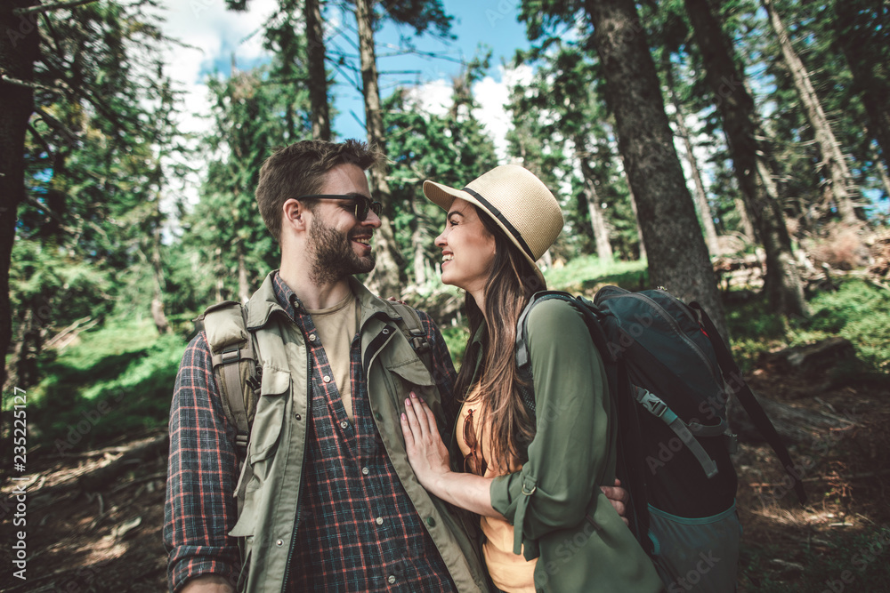 Concept of life activity in couple. Waist up portrait of happy man and woman looking to each other while standing together uphill in forest