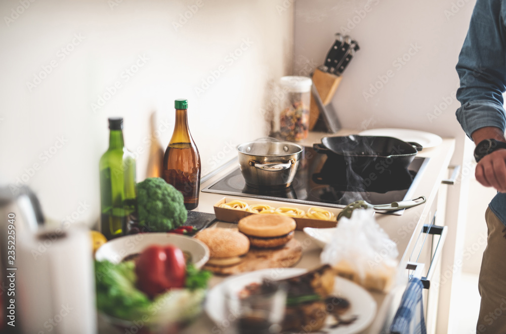 Kitchen desk with pasta, burger buns, vegetables and olive oil. Small pot and frying pan on stovetop Kitchen desk with pasta, burger buns, vegetables and olive oil. Small pot and frying pan on stovetop