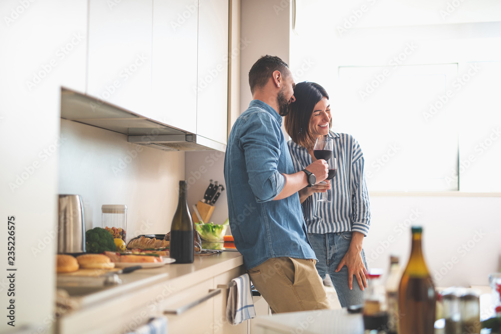Romantic date at home. Portrait of happy bearded man and his girlfriend holding glasses of wine while talking and laughing Romantic date at home. Portrait of happy bearded man and his girlfriend holding glasses of wine while talking and laughing