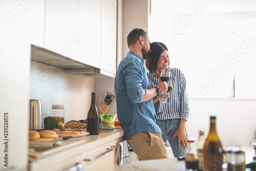 Romantic date at home. Portrait of happy bearded man and his girlfriend holding glasses of wine while talking and laughing