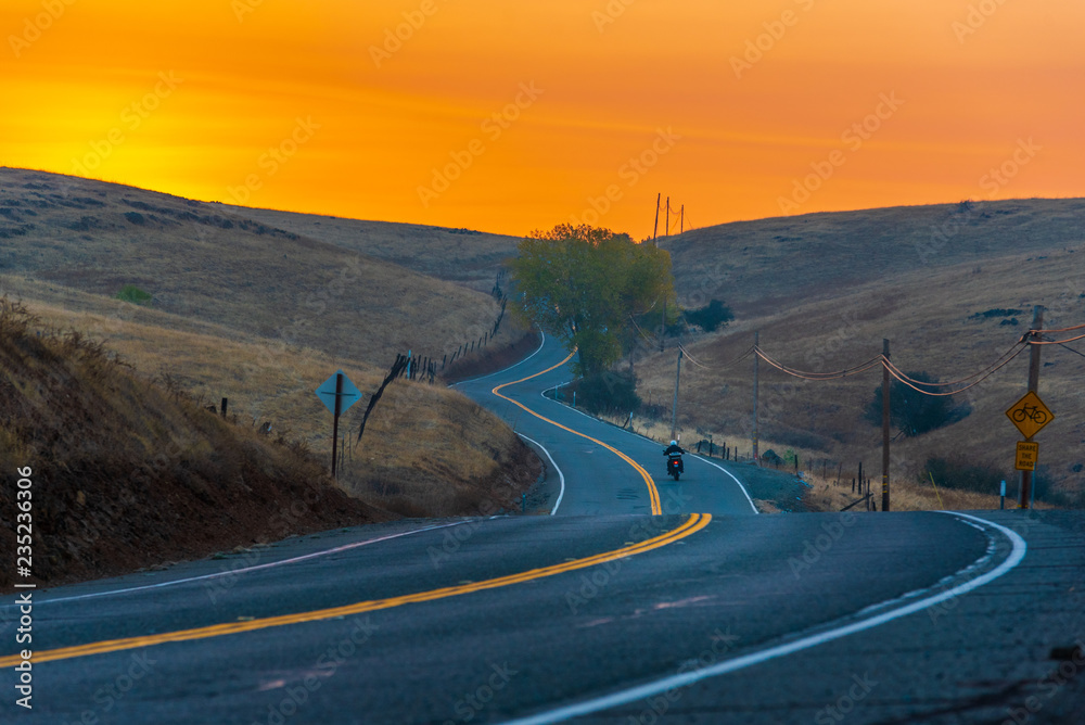 Motorcycle traveling down a winding country road at sunrise.