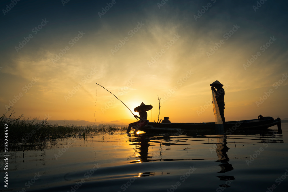 Silhouette of fishermen using nets to catch fish at the lake in Thailand morning light.
