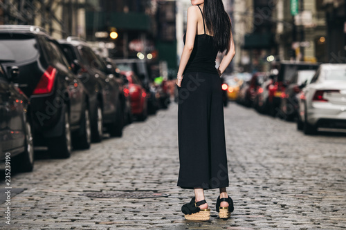 Female casual classic black style outfit with pants, top and shoes on city street