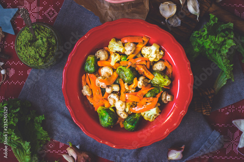 Baked roasted vegetables for Christmas lunch or dinner on red tablecloth. Vegan food with brussels sprouts, carrots, cauliflower, mushrooms. Social network trendy color style. In red bowl or plate