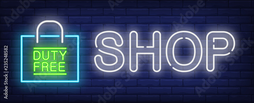 Shop neon sign. Glowing inscription with duty free paper bag on brick wall background. Can be used for airport, shopping, duty free zone