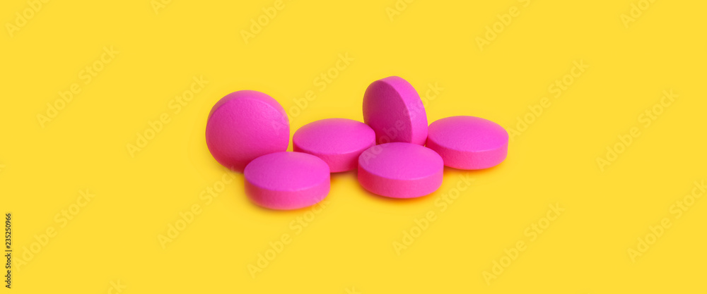 Several large pink tablets scattered on a yellow background. Side view. Several large pink tablets scattered on a yellow background. Side view.