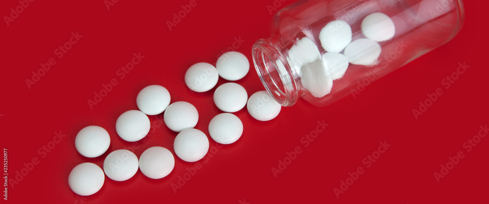 White tablets scattered from a glass jar on a red background. View from above. White tablets scattered from a glass jar on a red background. View from above.