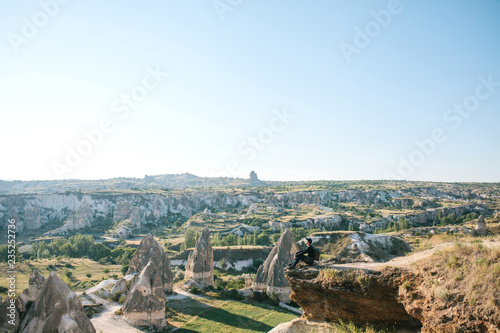 A man with a backpack or a tourist sits on top of a hill in Cappadocia in Turkey and meditates or seeks the soul or spends time in solitude.