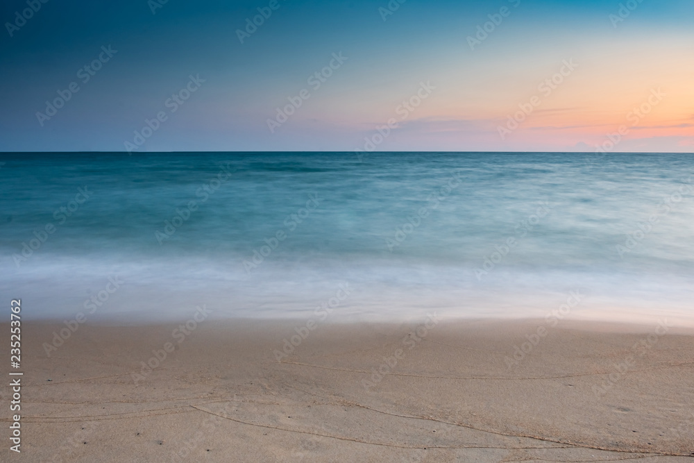 soft wave at sea beach on blue sky and orange sun set, long exposure shot