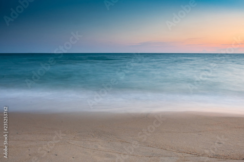 soft wave at sea beach on blue sky and orange sun set, long exposure shot