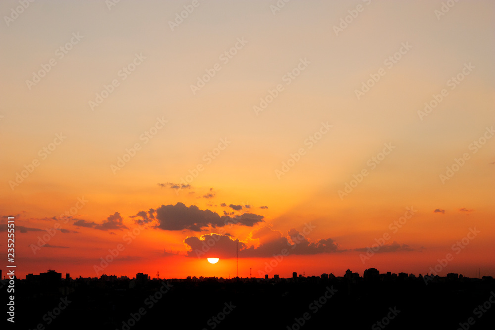 Sun hanging from cloud above backlit city skyline in big general shot and aerial view