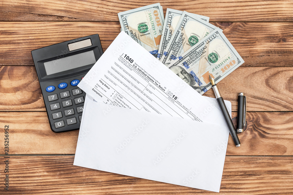 Tax form in envelope, with calculator, money and pen on wooden table. Business and tax concept. Top view. Tax form in envelope, with calculator, money and pen on wooden table. Business and tax concept. Top view.