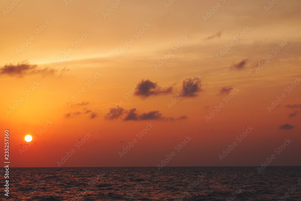 Beautiful serene view of sun setting during dusk over sea horizon with orange pastel sky 