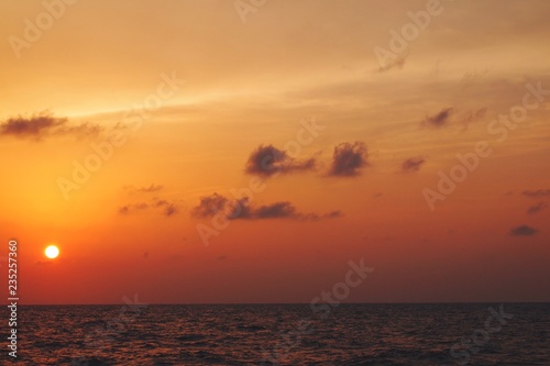 Beautiful serene view of sun setting during dusk over sea horizon with orange pastel sky  © teriztdh
