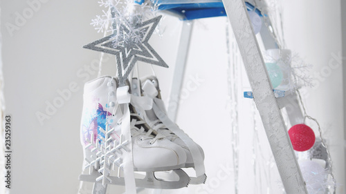 Close up of pair of white figure skates hangs on decorated stepladder. Christmas concept